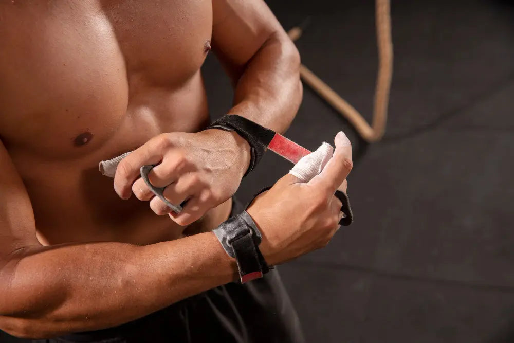 Homem com tronco musculoso ajustando straps de treino nas mãos antes de exercício de força.
