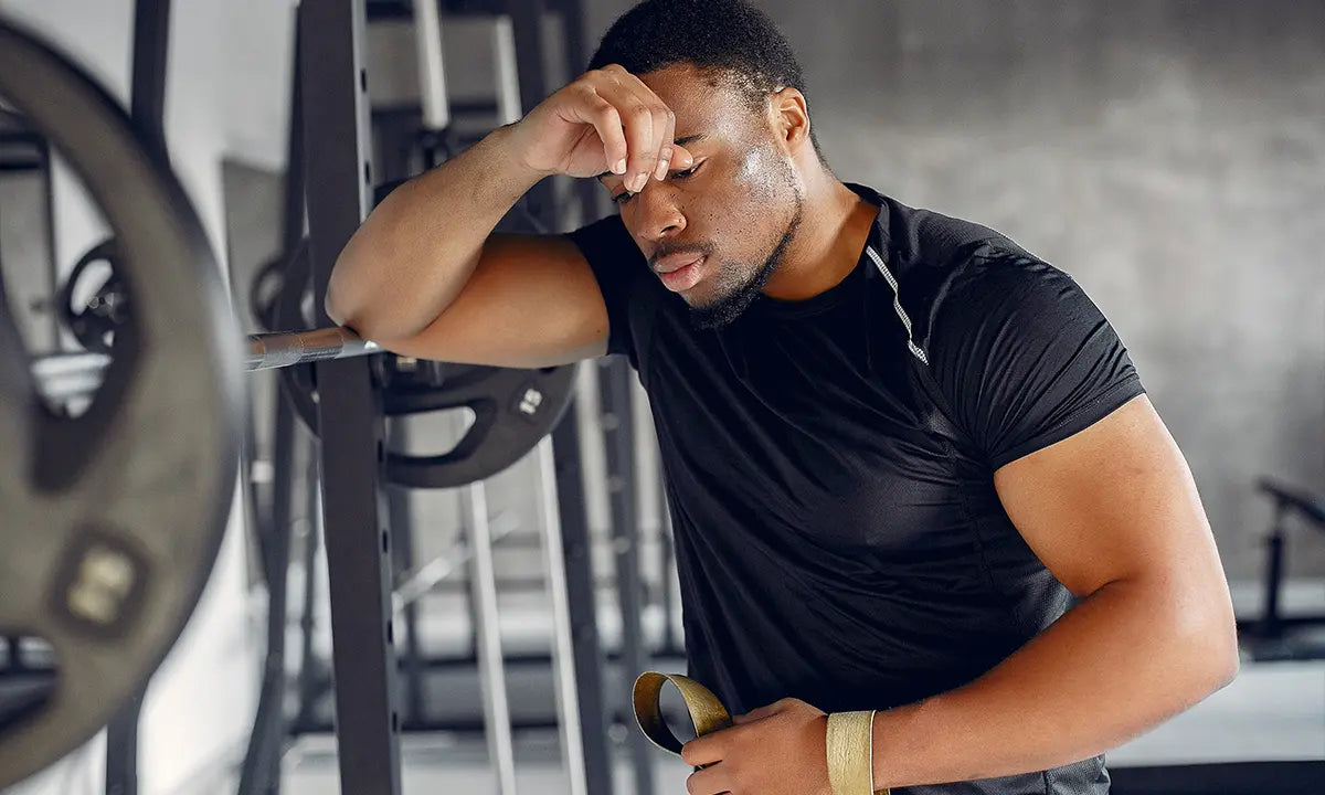 Homem cansado e com overtraining apoiado em equipamento de musculação na academia.