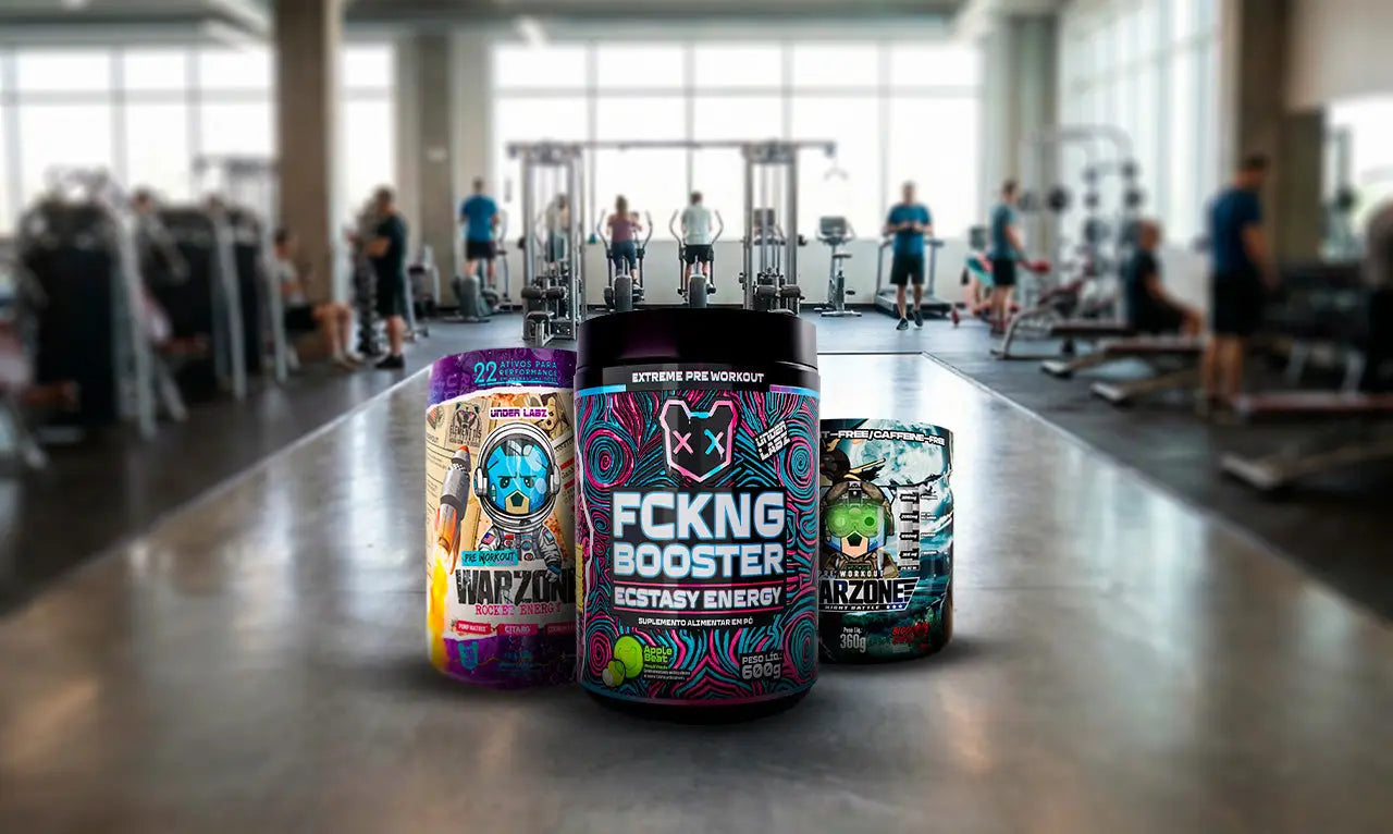 Três potes de suplemento pré-treino em destaque no centro de uma academia. Ao fundo, pessoas treinam em aparelhos, mas o foco é nas embalagens coloridas e chamativas dos produtos.